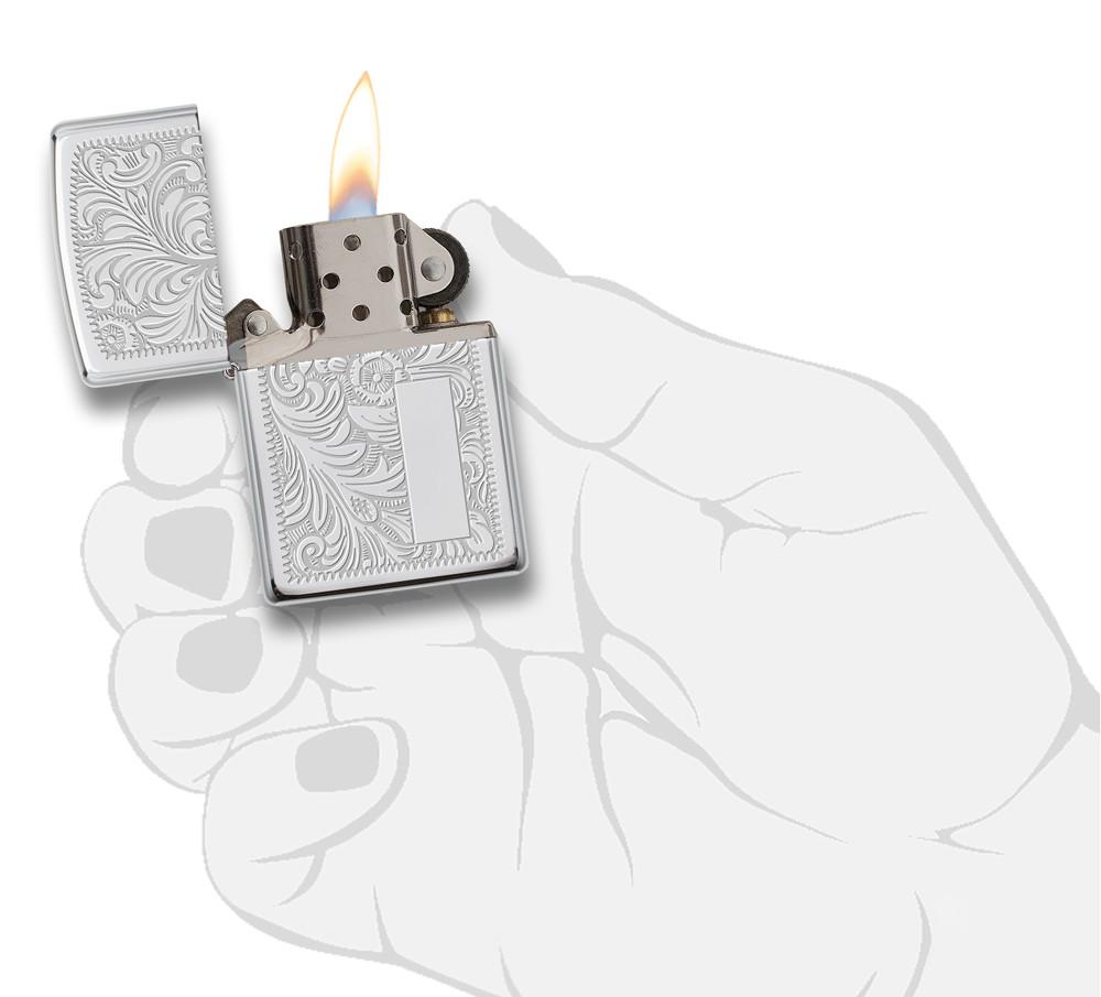 Vue de face briquet Zippo High Polish Chrome avec motif vénitien et plaque à graver, ouvert avec flamme dans une main stylisée