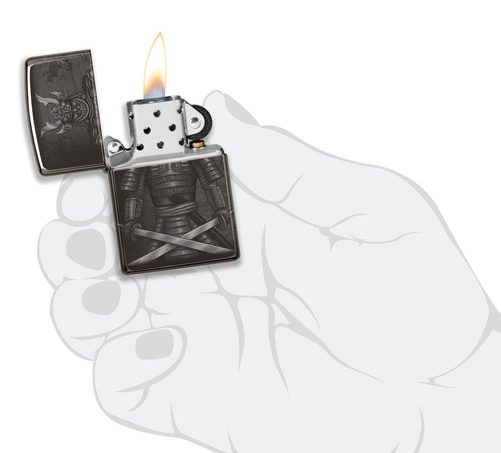 Vue de face briquet Zippo noir brillant avec samouraï et épées croisées, ouvert avec flamme dans une main stylisée