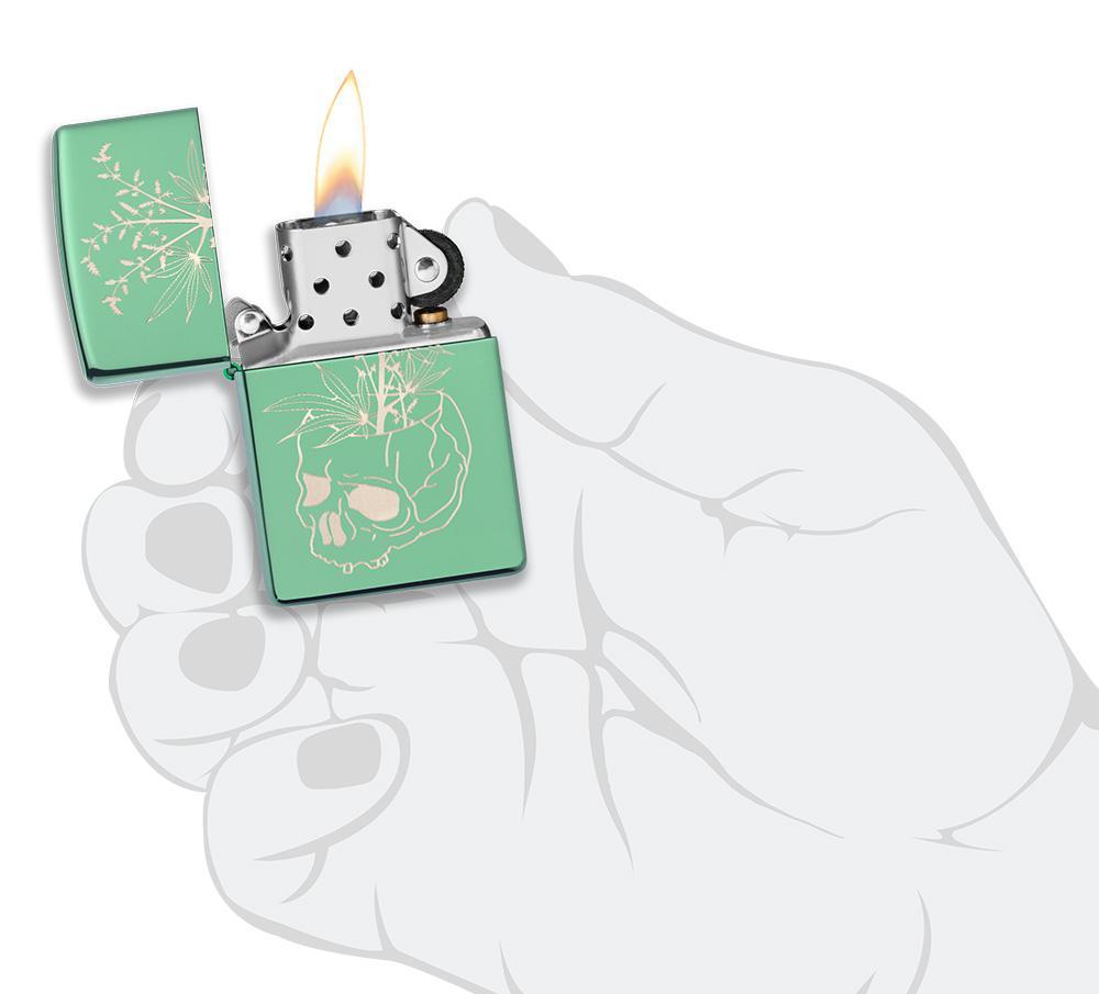 Briquet Zippo vert brillant tête de mort servant de pot à un plant de chanvre, ouvert avec flamme dans une main stylisée