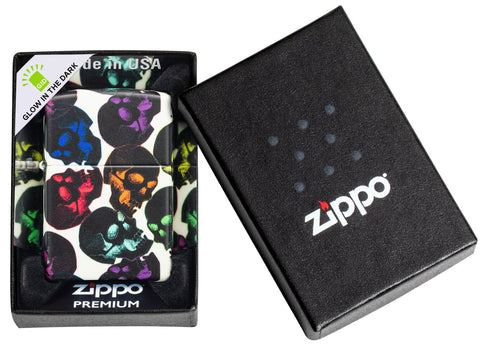 Encendedor Zippo vista frontal Diseño de calaveras con algunas calaveras multicolores brillando en la noche en su caja negra premium