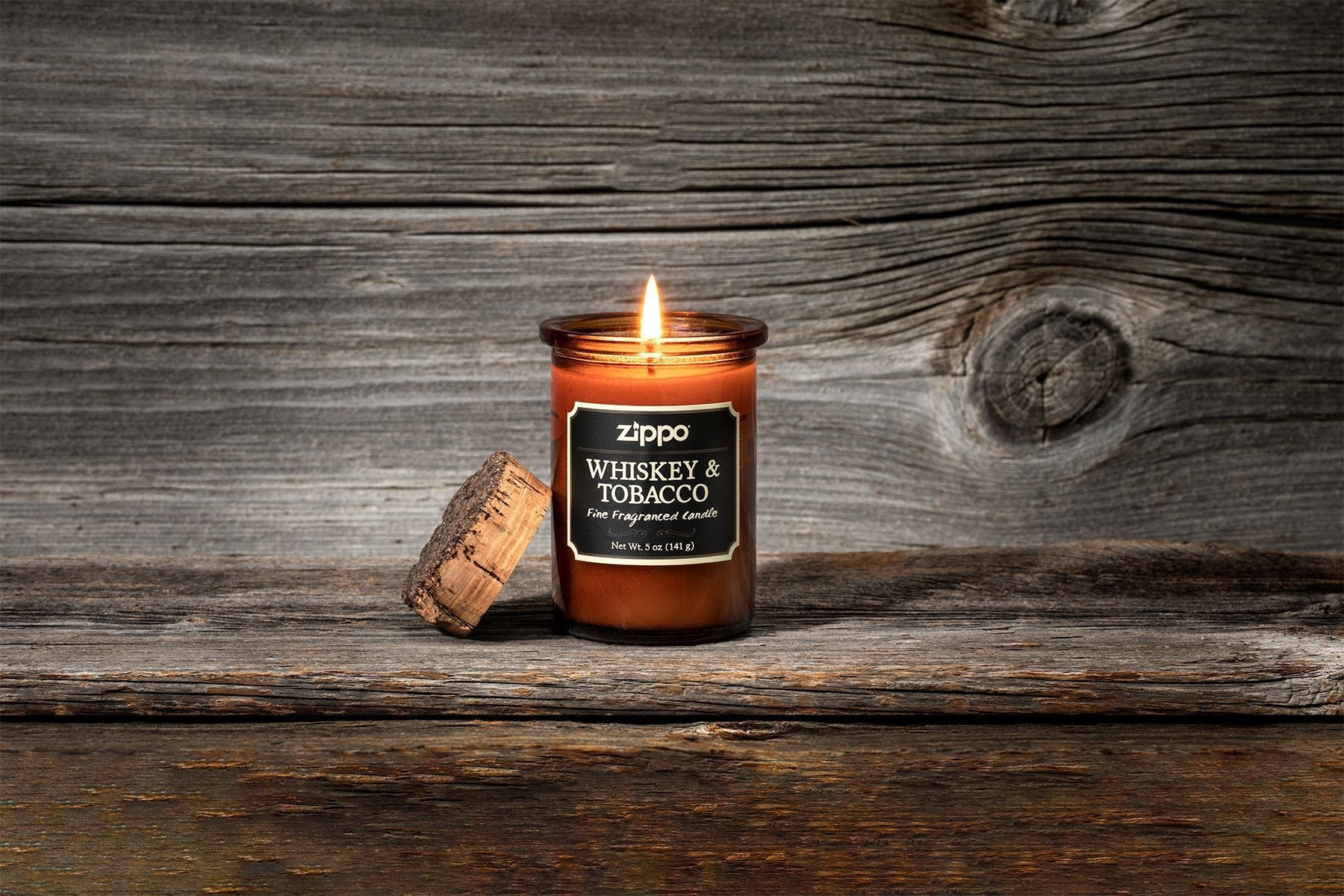Bougie Zippo Whiskey and Tobacco marron avec couvercle en liège, avec flamme devant un arrière-plan en bois