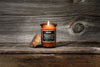 Bougie Zippo Whiskey and Tobacco marron avec couvercle en liège, avec flamme devant un arrière-plan en bois