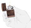 Vue de face briquet Zippo Armor Antique Copper Multi Cut avec gravure carte du monde, ouvert avec flamme dans une main stylisée