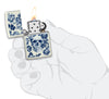Encendedor Zippo que brilla en la oscuridad calavera con corona rodeada de flores azules abierta con llama en mano estilizada