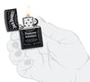 Vue de face briquet Zippo noir mat avec logo Jack Daniel's, ouvert avec flamme dans une main stylisée