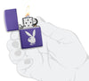 Vue de face briquet Zippo imprimé texturisé violet mat avec logo lapin Playboy, ouvert avec flamme dans une main stylisée